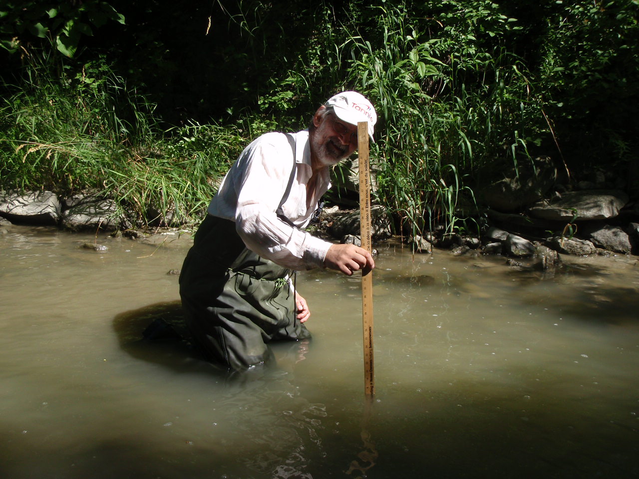 A man in chest waders measures water depth with a metre stick