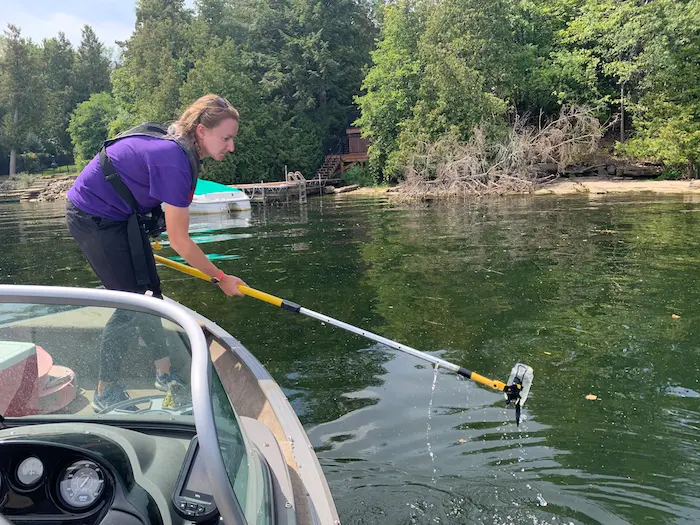 A woman uses a long pole to sample water from a boat